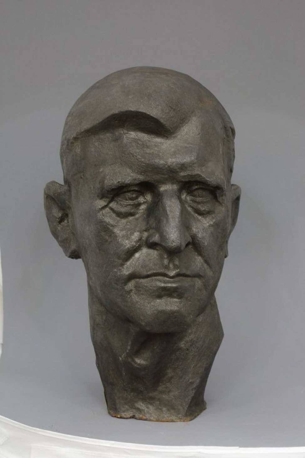 Скульптурное изображение головы пожилого мужчины. Голова в фас с крупным носом, плотно сжатыми губами с нависшими на глаза надбровными дугами. Гладкие волосы зачесаны на правую сторону.