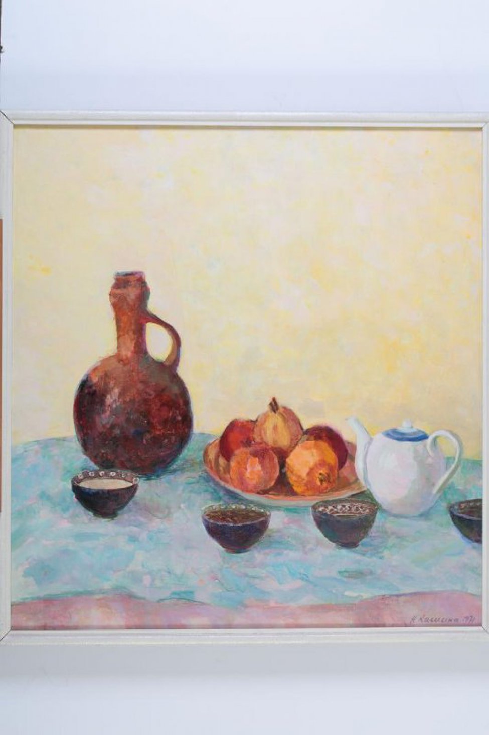 На светлом фоне натюрморт: на светло-голубой скатерти 4 пиалы, белый чайник; в глубоком блюде - гранаты.