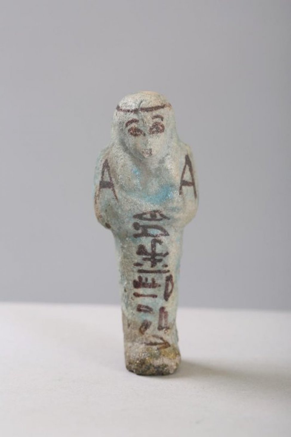 Изображена фигурка человека в виде запеленутой мумии с нарисованными глазами и иероглифами на туловище.