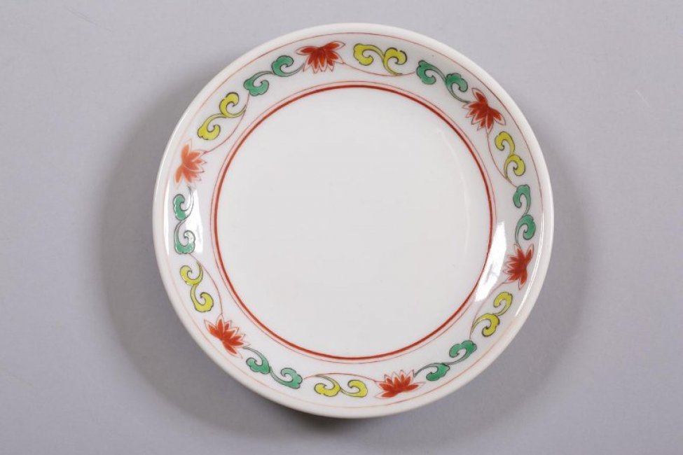 Блюдце чайное, круглое, мелкое, белое с росписью по борту: красные цветы, соединённые орнаментом из жёлтых и зелёных завитков.