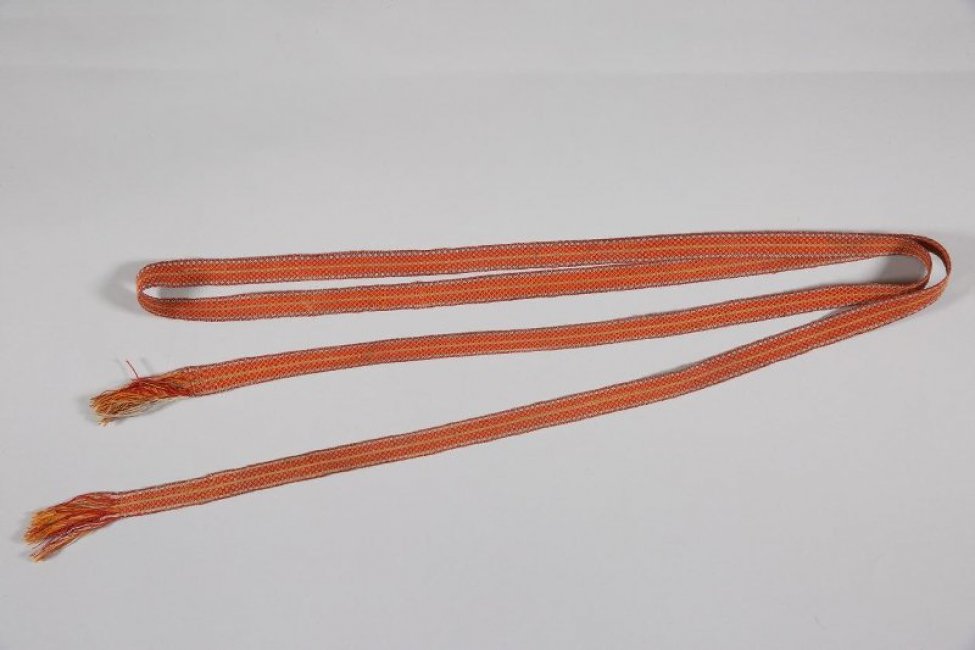 Заткан узором из мелких ромбиков с точкой посередине, выполненным красными и оранжевыми нитями. Вдоль пояса - три узкие полоски (синий с белым и зеленый с желтым цвета). На концах длинная бахрома (ко. 5,5 см).